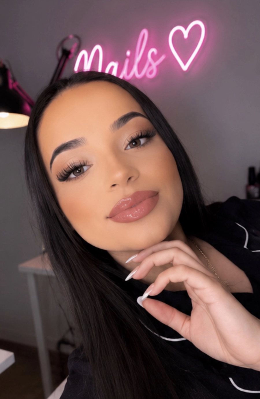 Omi in her nail lounge, under her neon Nails sign